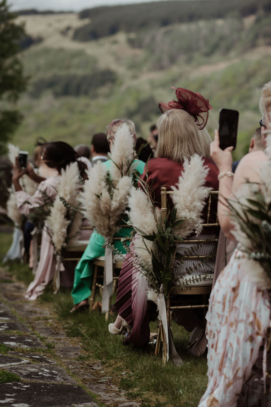 Pampas grass decorated chairs with guests by White Heather Wedding & Event Planning Services